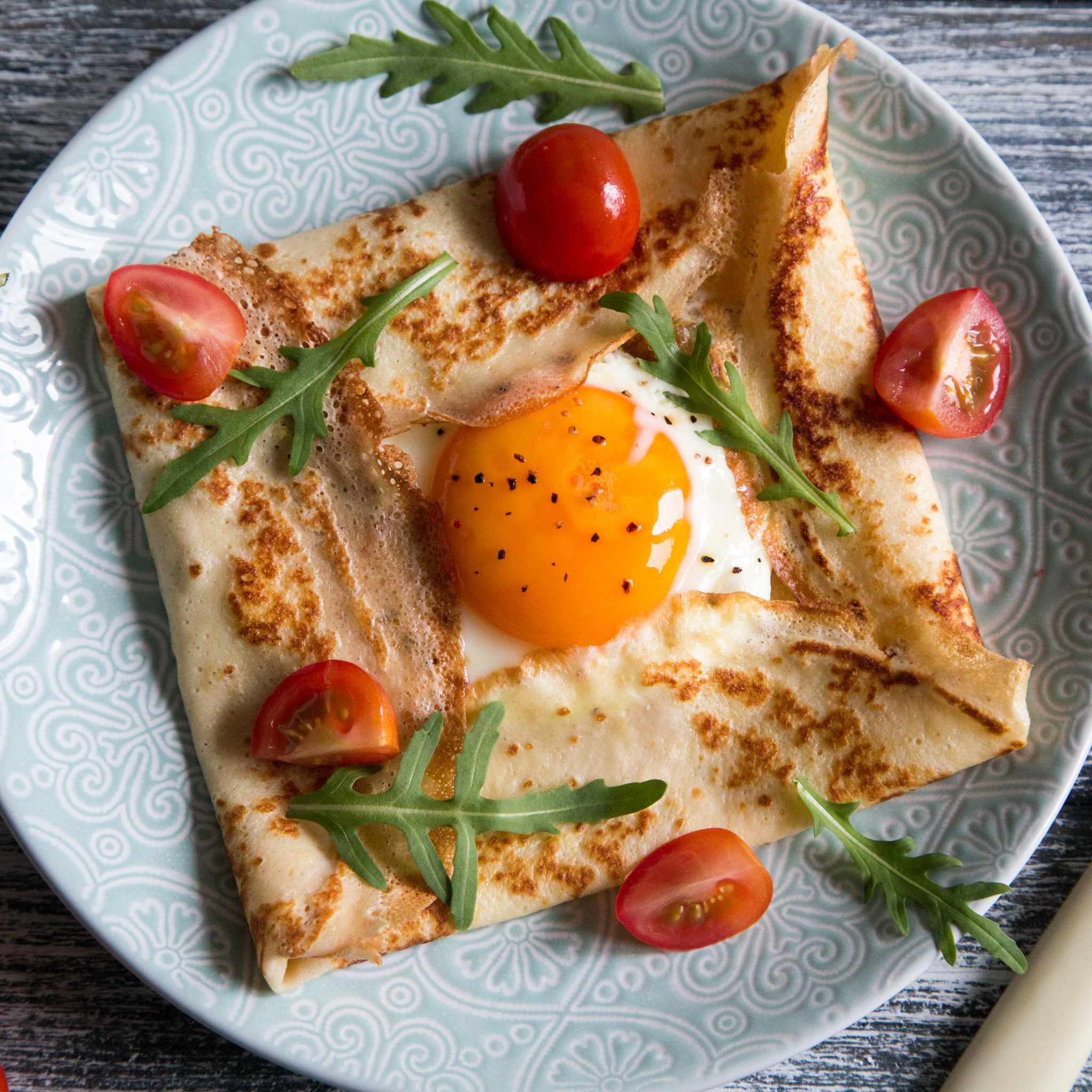Savoury breakfast crepe filled with egg and scattered with chopped cherry tomatoes and rocket