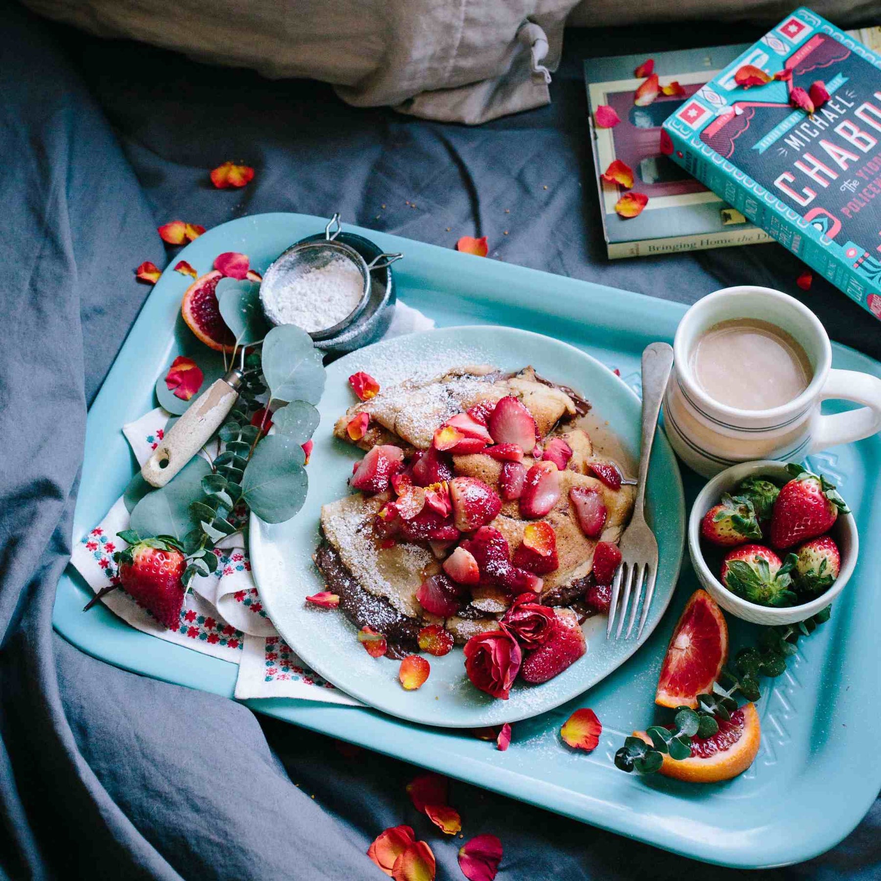 Breakfast tray with fresh coffee and strawberry crepes, with a bowl of strawberries and red roses alongside