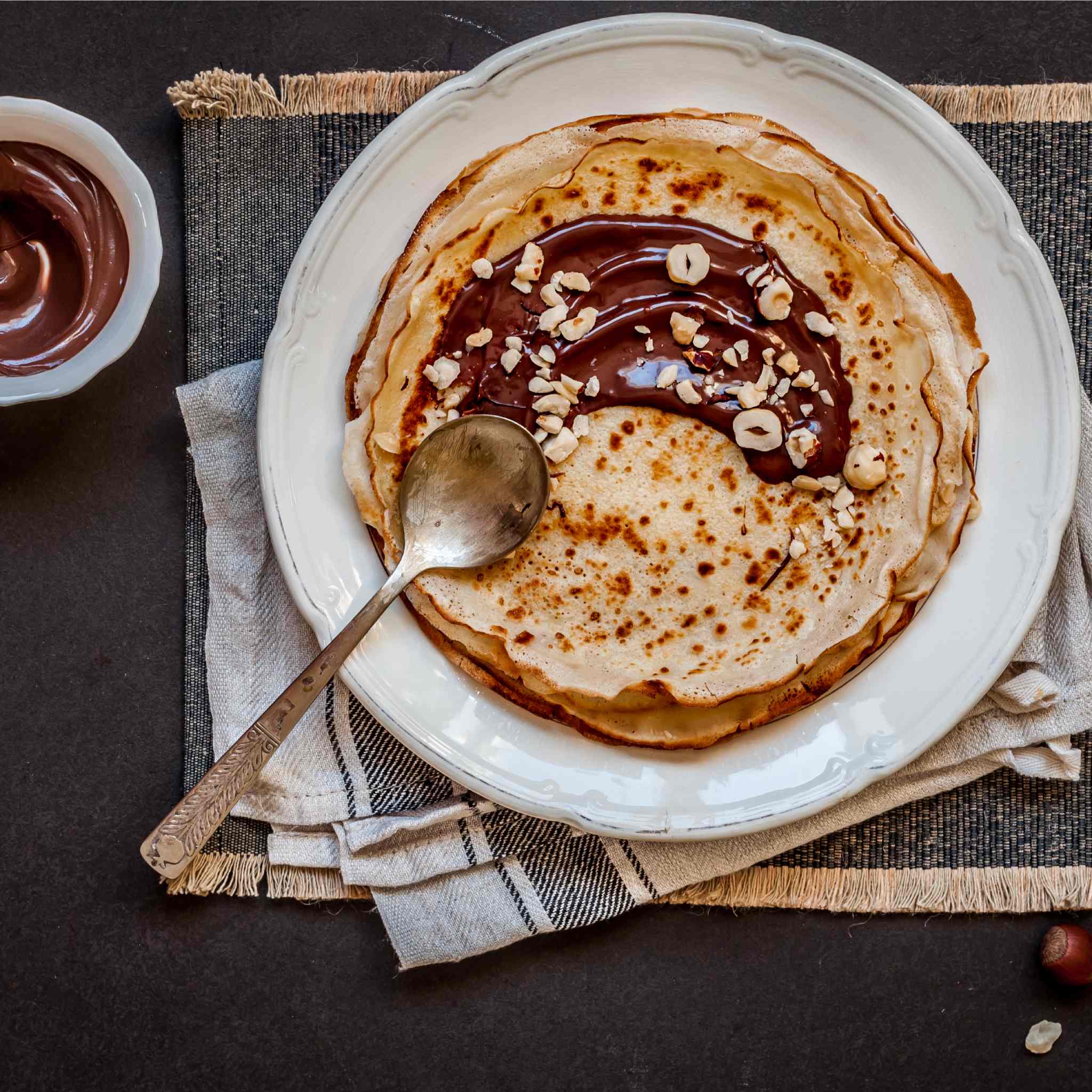 Stack of pancakes spread with Nutella and topped with crushed hazelnuts