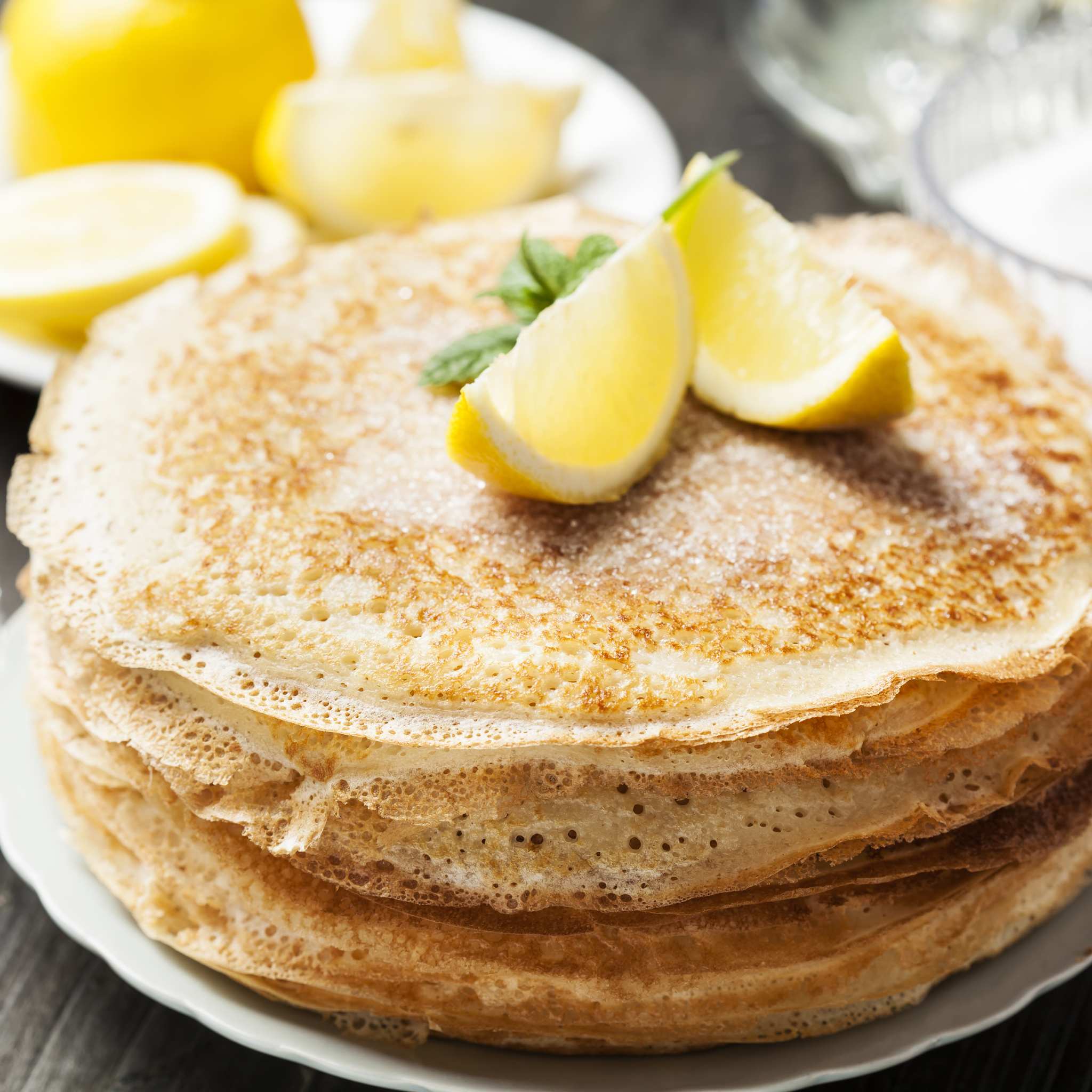 Stack of pancakes sprinkled with sugar and with wedges of lemon on top